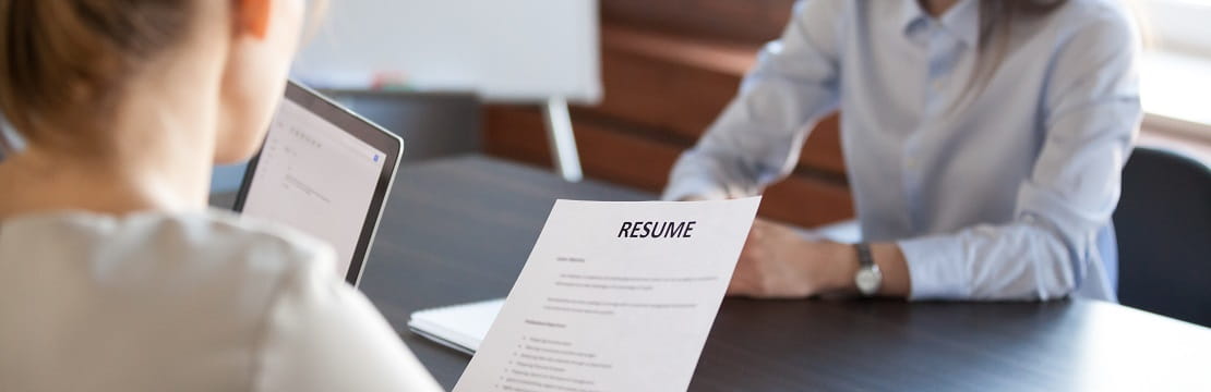 Two women professionals sit at an office table with a resume. 