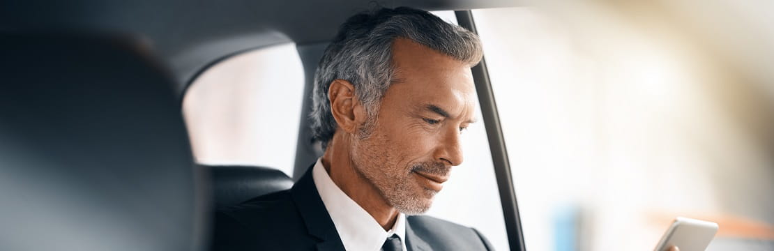 A business professional riding in a vehicle and looking at their phone