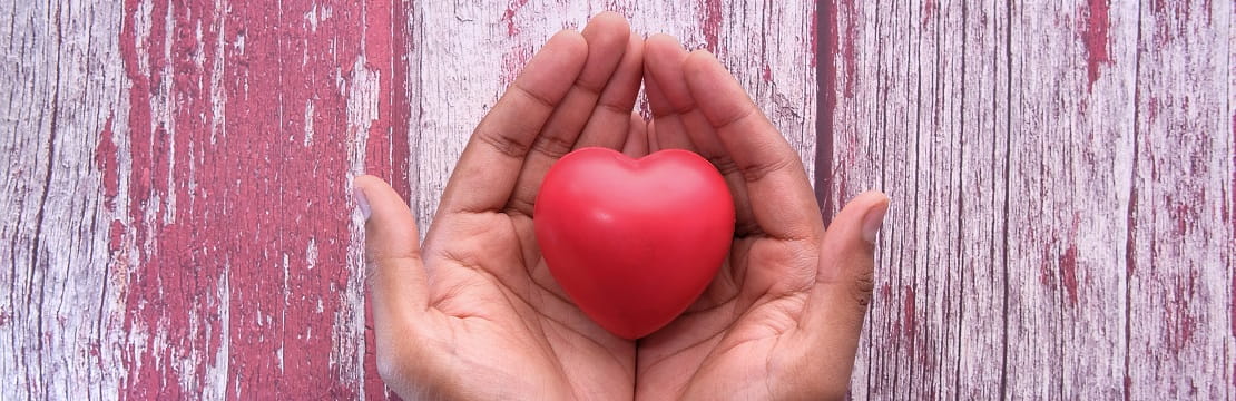 Hands holding a heart-shaped stress ball over a painted wood background. 
